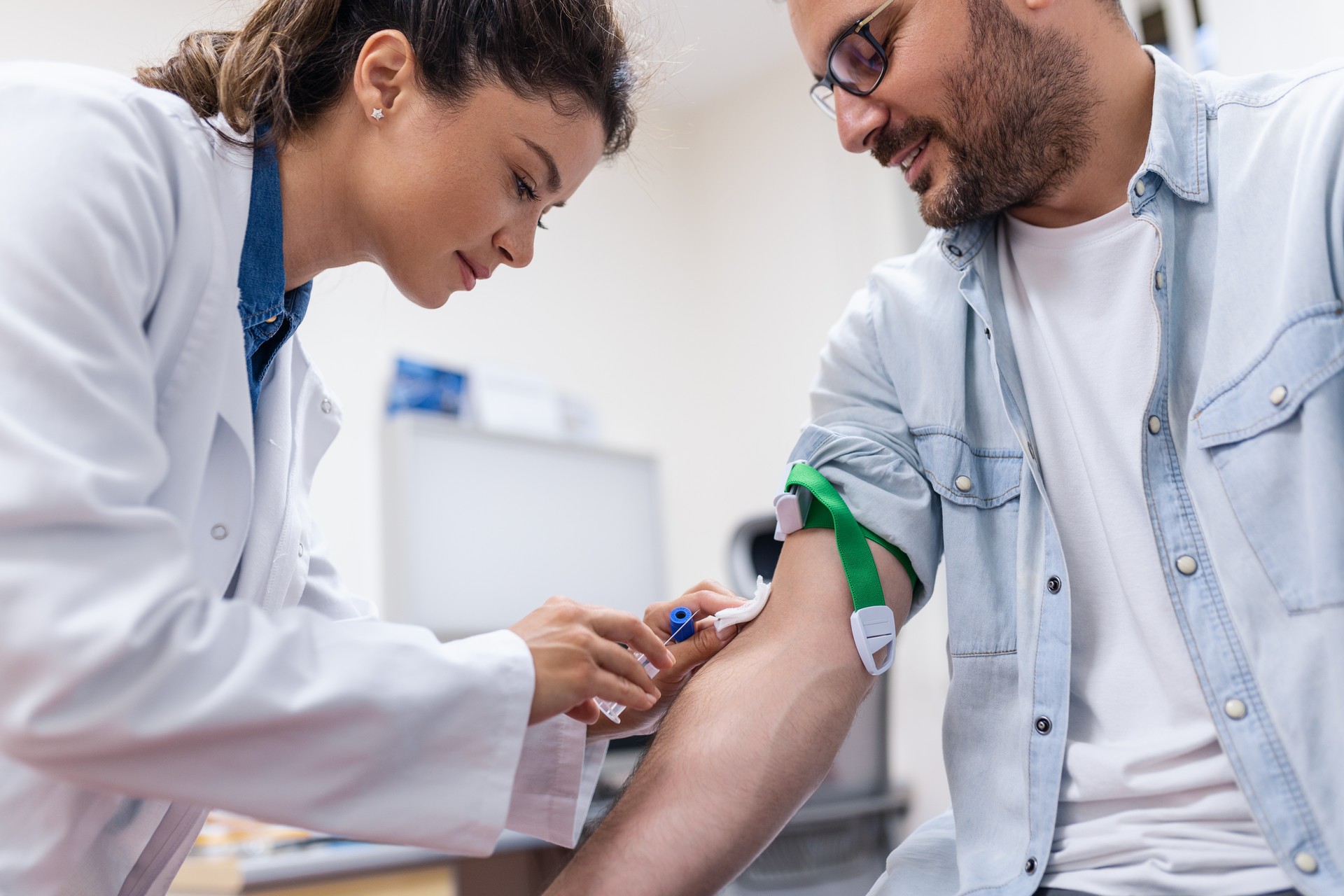 Preparation for blood test by female doctor medical uniform on the table in white bright room. Nurse pierces the patient's arm vein with needle blank tube.